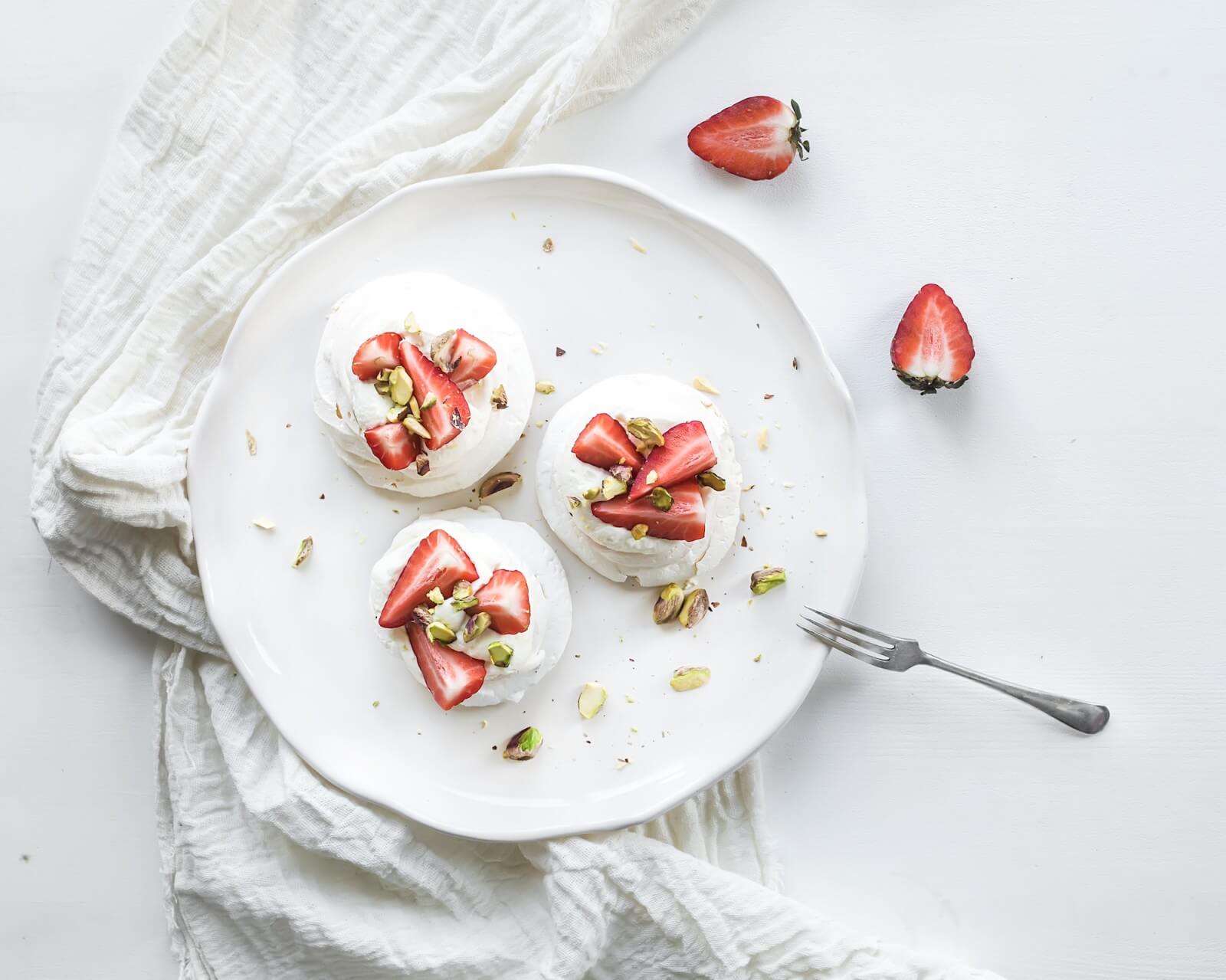 Small strawberry and pistachio pavlova meringue cakes with mascarpone cream, fresh mint over white backdrop, top view