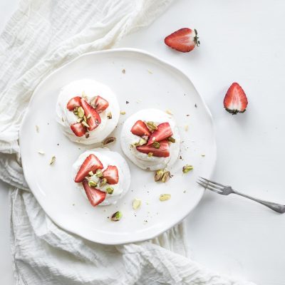 Small strawberry and pistachio pavlova meringue cakes with mascarpone cream, fresh mint over white backdrop, top view